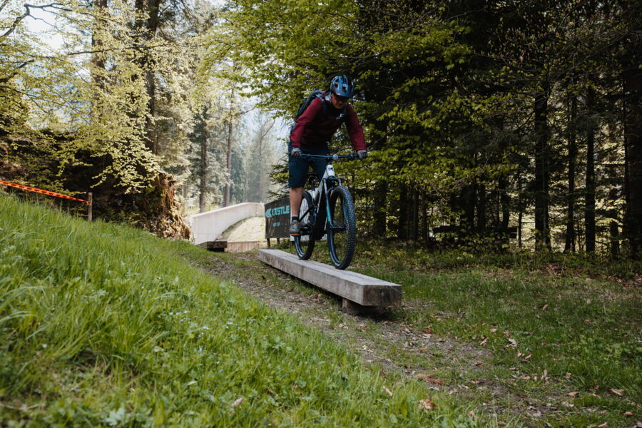 A mountain biker rides over a wooden beam on the mountain bike course in Hintersee.