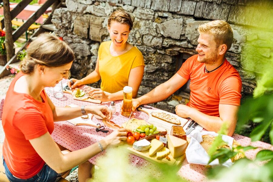 Zwei junge Frauen und ein junger Mann Essen gemeinsam eine Almjause mit Weintrauben, Tomaten, Käse und Brot.