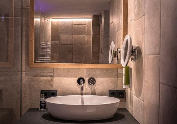 The elegantly designed washbasin and the large mirror above the tiled wall with natural stone look
