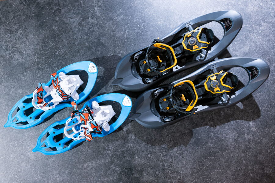 Ein Paar kleine blaue und ein Paar große grau-gelbe Schneeschuhe liegen auf dunklem Steinboden.