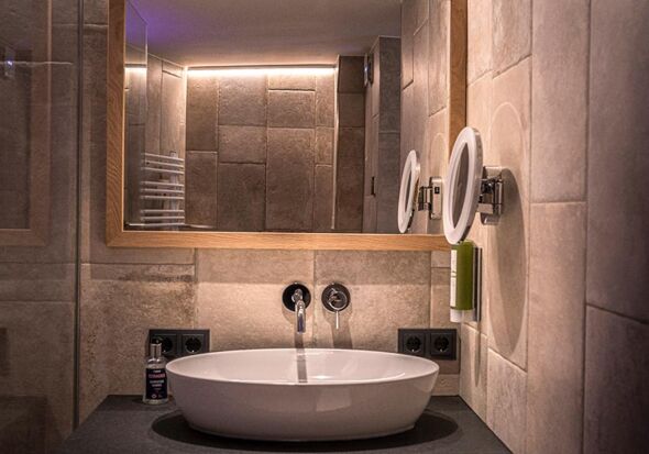 The elegantly designed washbasin and the large mirror above the tiled wall with natural stone look