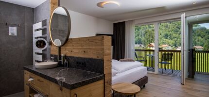 The large marble washbasin, the double bed and the glass front to the terrace of the luxurious chalet of Das Hintersee in Salzkammergut, Austria