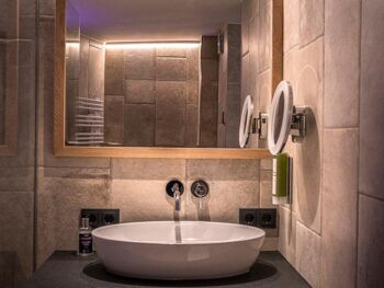 The elegantly designed washbasin and the large mirror above the tiled wall with natural stone look