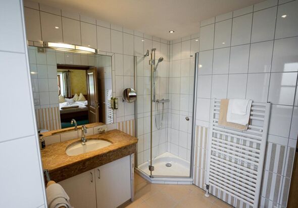 Das weiß geflieste Bad mit geräumiger Dusche
